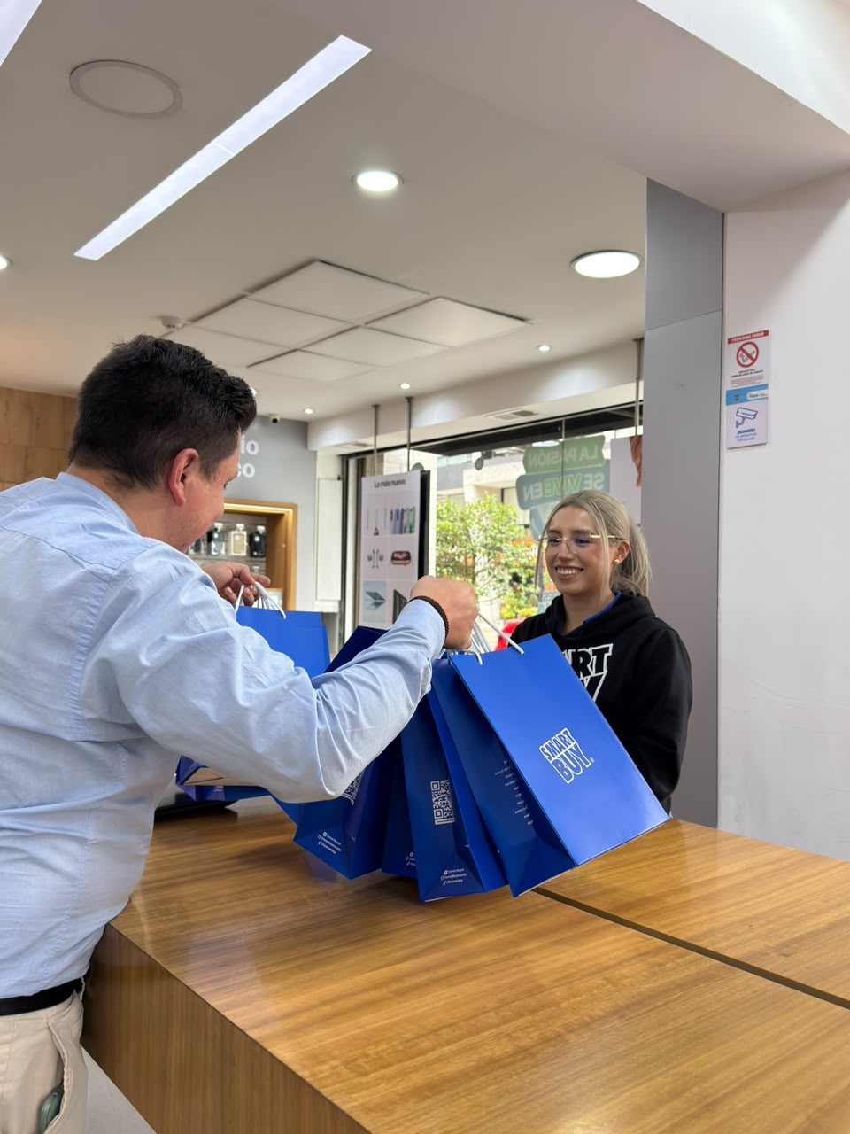 Asesora SmartBuy entregando bolsas con pedido de mayorista a un cliente en tienda